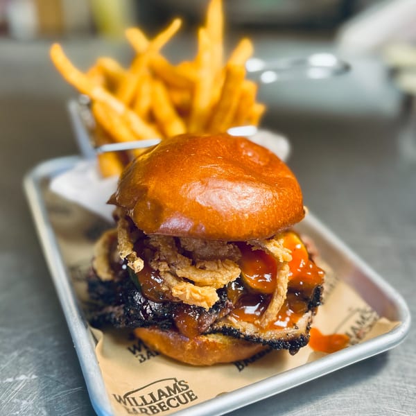 William's Barbecue brisket sandwich with crispy fried onions and barbecue sauce, served with fries.