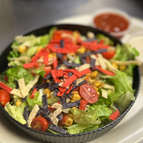 A vibrant William's Barbecue salad with lettuce, corn, tomatoes, and colorful tortilla strips.