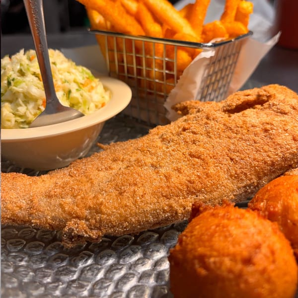 Fried fish fillet, hush puppies, coleslaw, and french fries on a textured plate.