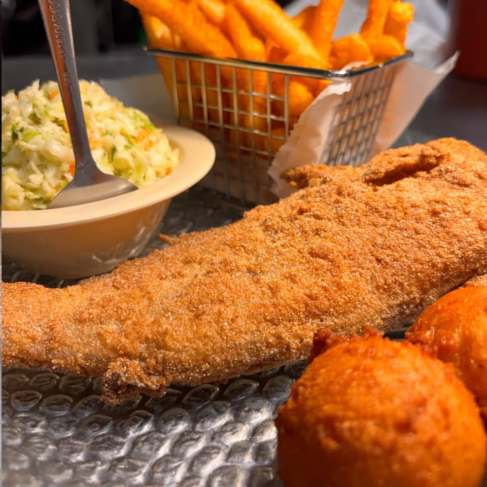 Fried fish fillet, hush puppies, coleslaw, and french fries on a textured plate.