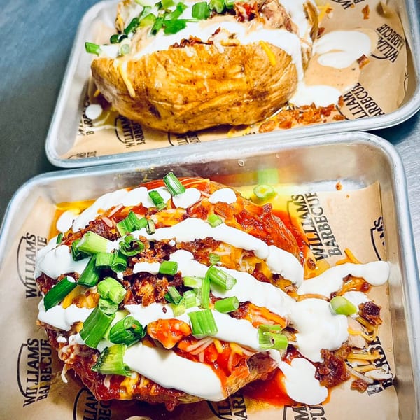 Two William's Barbecue loaded baked potatoes with cheese, sour cream, bacon, and green onions.