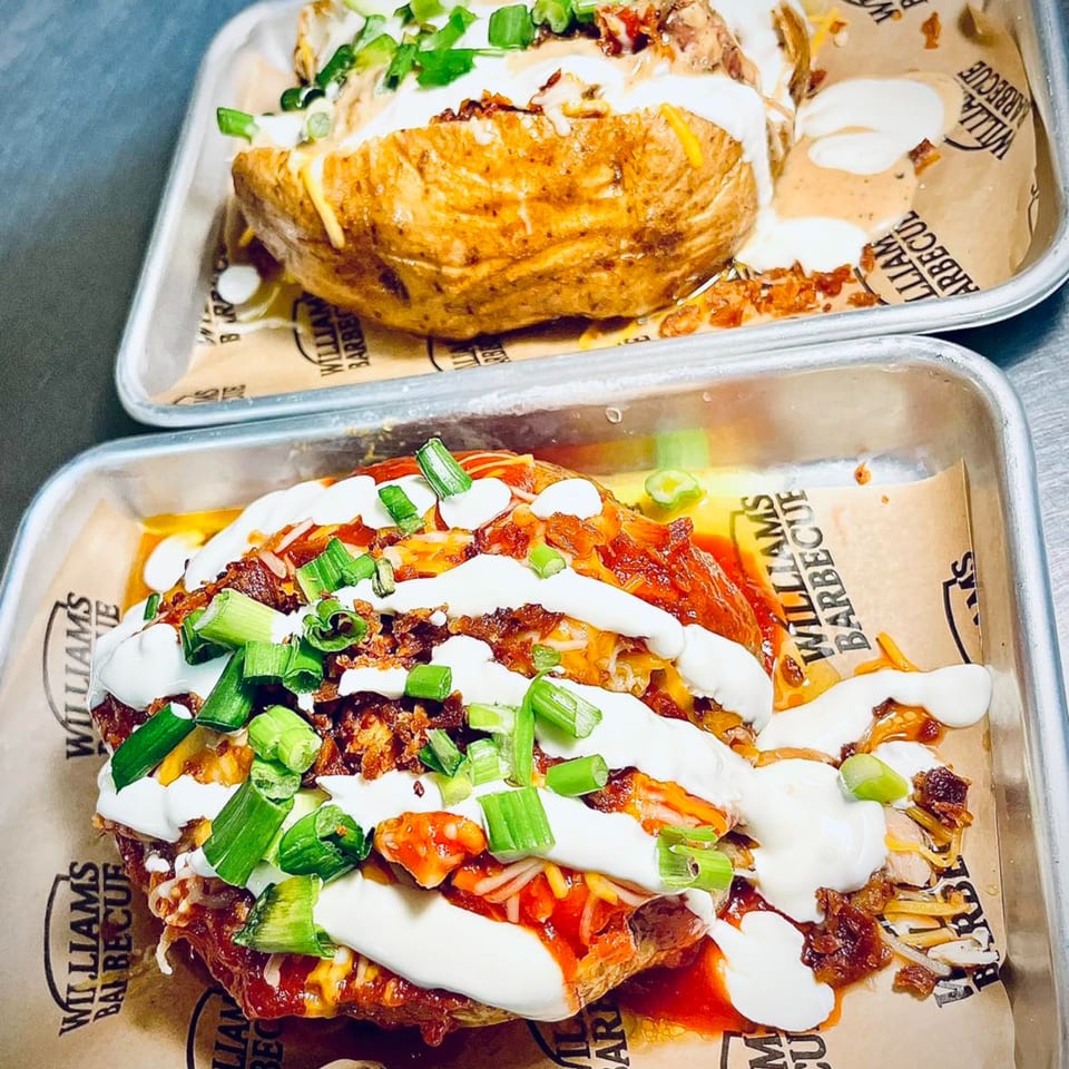 Two William's Barbecue loaded baked potatoes with cheese, sour cream, bacon, and green onions.