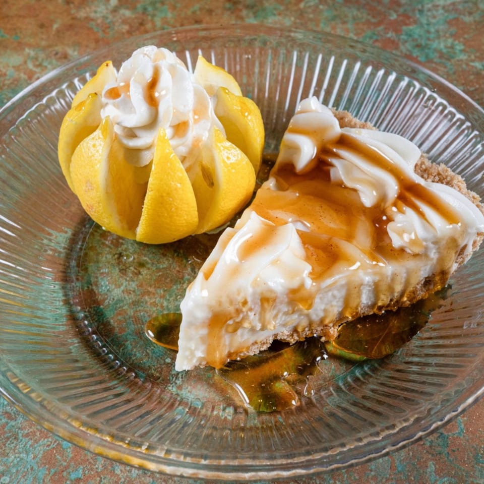 A slice of pie with whipped cream and caramel drizzle, next to a lemon cup with whipped cream.