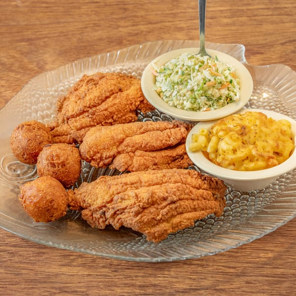 William's Barbecue fried fish, hush puppies, coleslaw, and macaroni and cheese on a clear plate.