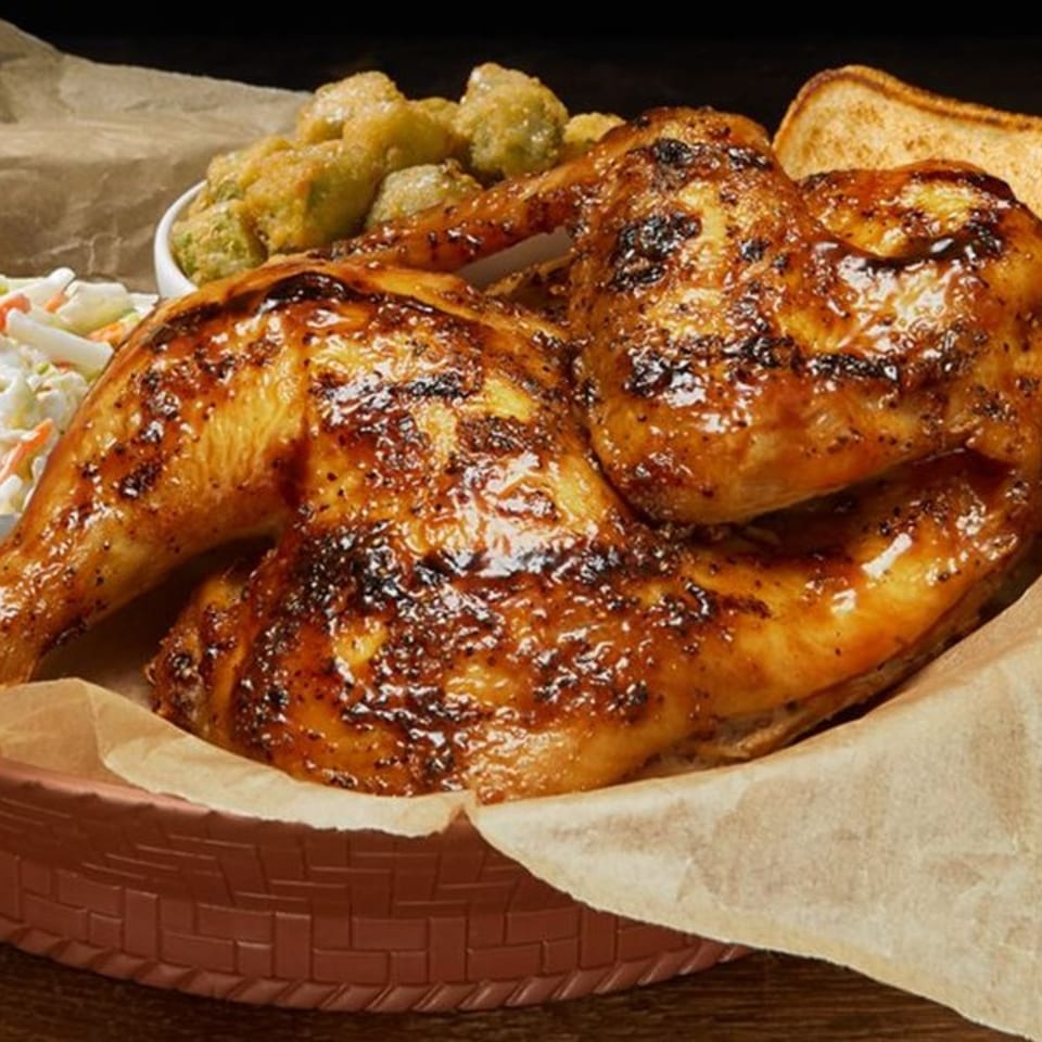 Half a grilled chicken with crispy skin, coleslaw, fried okra, and toast in a basket.