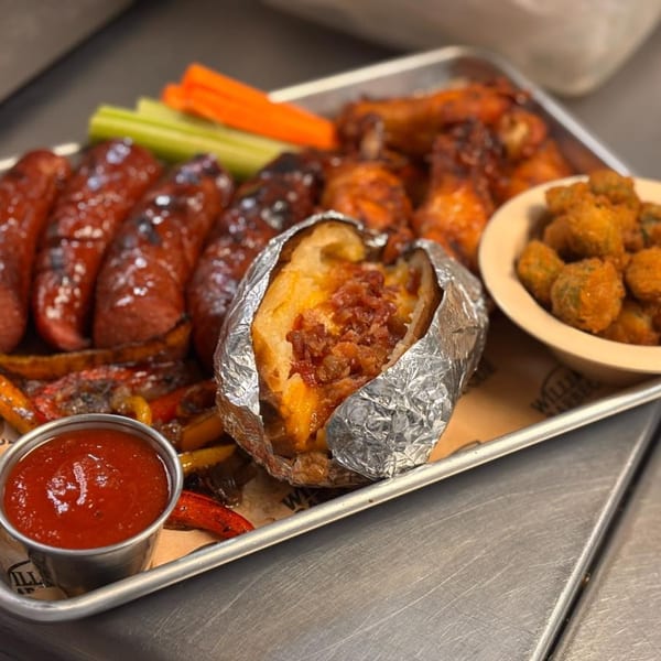 William's Barbecue platter with sausages, wings, loaded baked potato, fried okra, and dipping sauce.