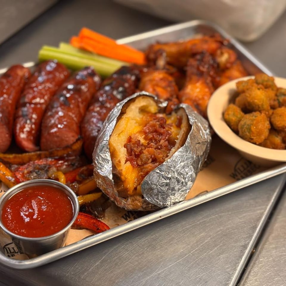 William's Barbecue platter with sausages, wings, loaded baked potato, fried okra, and dipping sauce.