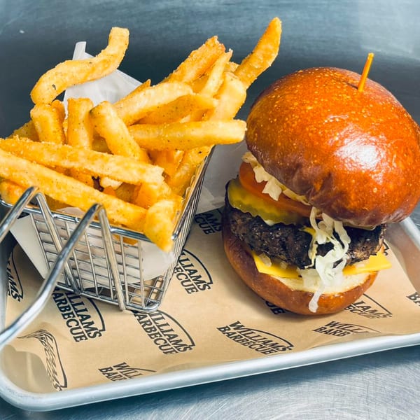 William's Barbecue burger with cheese, lettuce, tomato, and pickles, served with a side of fries.