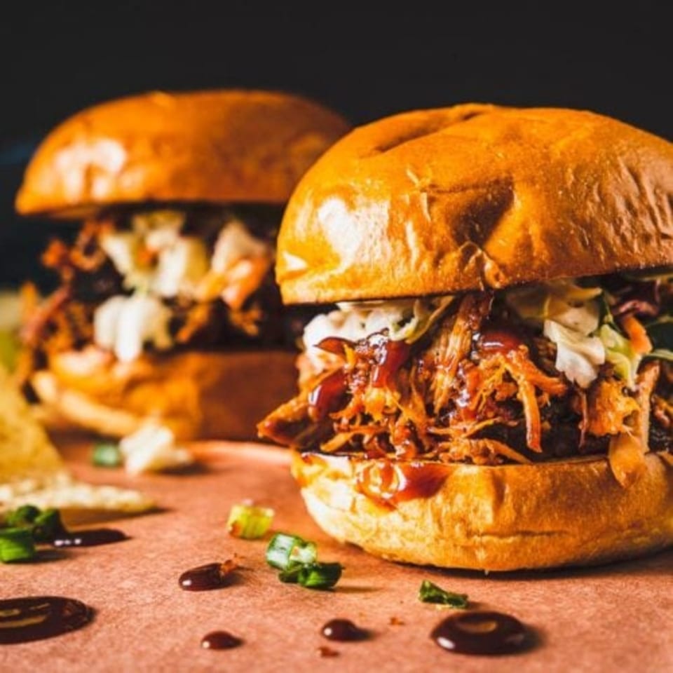 Two pulled pork sandwiches with coleslaw and BBQ sauce on buns, with scattered green onions.